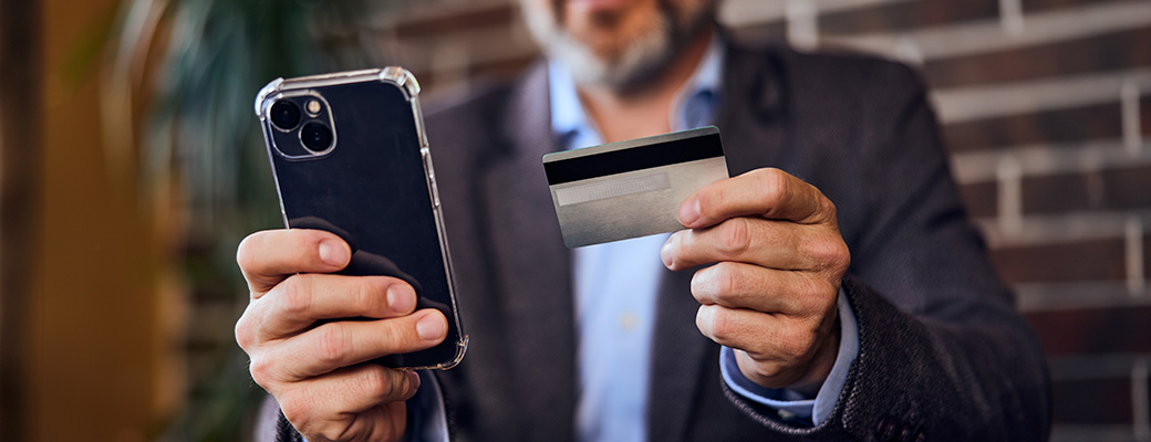 Hombre de mediana edad sujetando su teléfono móvil en una mano y una tarjeta bancaria en la otra